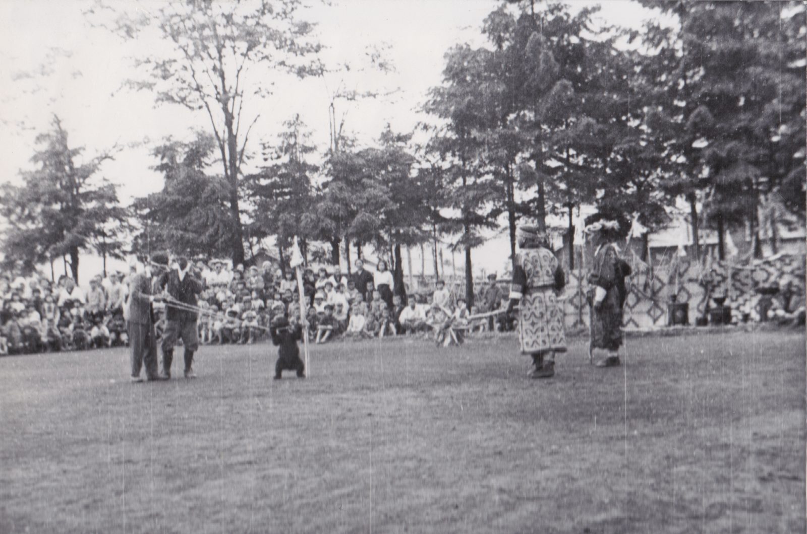 芝生の上で着物を着て輪になって踊る人物とそれを見る観衆。
