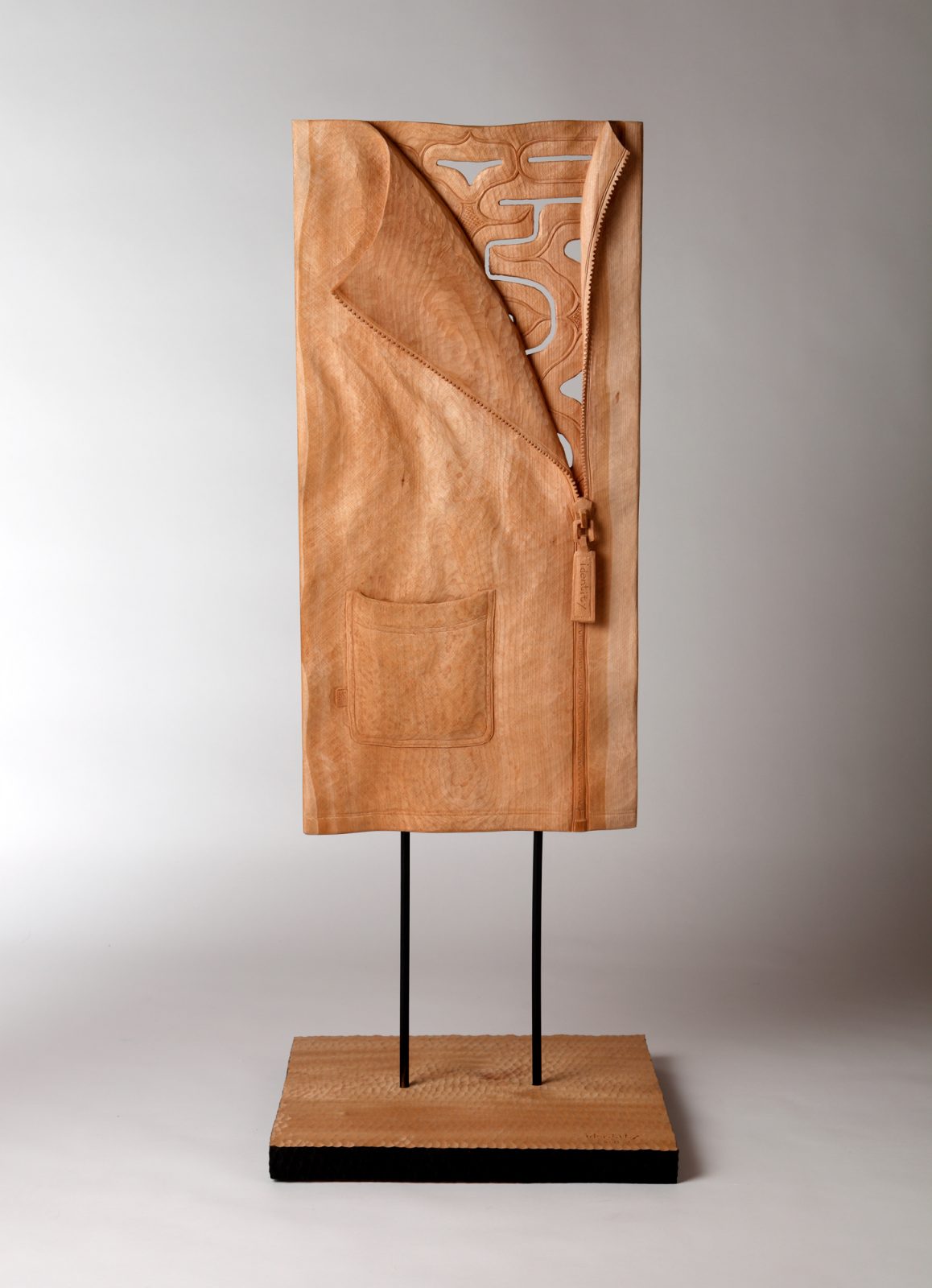 衣類のファスナーをひらいた内部からアイヌ文様がのぞいている木彫作品